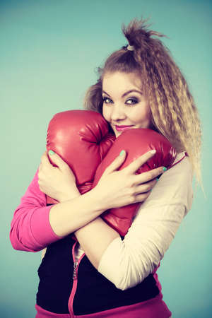 Funny cute blonde girl female boxer with big fun red gloves playing sports boxing studio shot on blueの写真素材