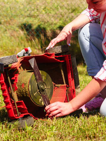 Gardening. Female person gardener mowing green lawn with lawnmower, having problem with broken mowerの写真素材