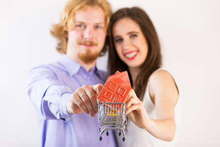 Man and woman, happy couple, showing house in shopping cart presenting buying new home plan concept.