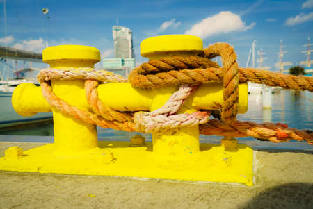 Shipping objects concept. Sailing ropes tied around yellow marina bollard. Outdoor shot on sunny day.の写真素材
