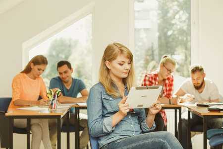 Education, high school, digital online learning concept - student girl with tablet pc computer sitting in front of students her group mates in classroomの写真素材