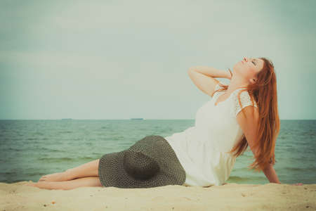 Summertime outfit accessories concept. Happy redhead woman wearing big black sun hat lying on beach...