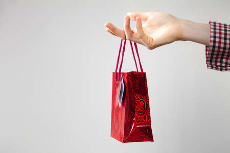 Unrecognizable woman hand holding red gift shopping bag for present. Studio shot on greyの写真素材
