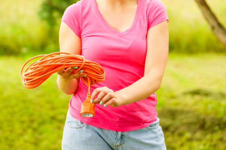 Young blonde woman holding work tool rolling up cable garden extension cord.