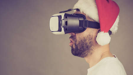 Man wearing santa claus hat exploring space with virtual reality goggles headset, vr box. Cyber...