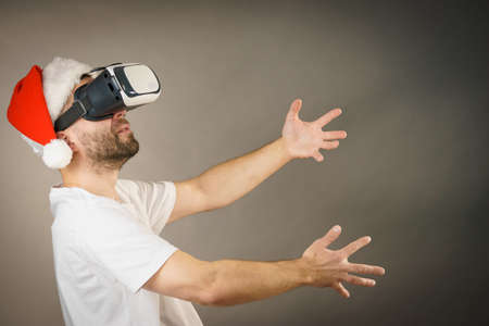 Man wearing santa claus hat exploring space with virtual reality goggles headset, vr box stretching...