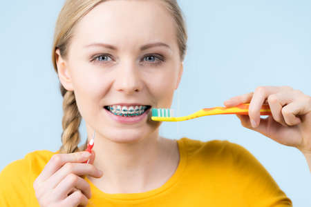 Dentist and orthodontist concept. Young woman smiling cleaning and brushing teeth with braces using toothbrushの写真素材