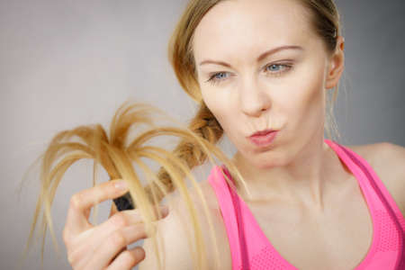 Happy woman looking at her long blonde hair ends, seeing positive effects of using conditioner....