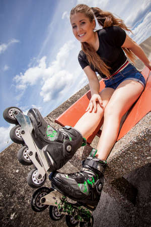 Happy joyful young woman wearing roller skates sitting in town. Female being sporty having fun during summer time.の写真素材