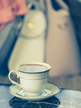 Elegant retro styled coffee cup on wooden table, colorful purse bags in background.の写真素材