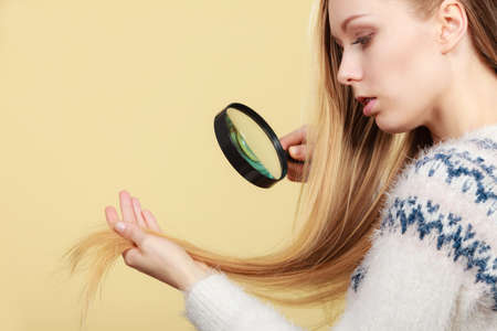 Haircare, health problem concept. Unhappy blonde woman looking at ends of her blonde hair through...