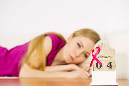 Woman lying on bed looking at calendar, it is 4 february world breast cancer day, date with pink awareness ribbon. Healthcare and medicine concept.の写真素材