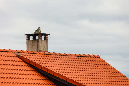 Architecture concept. Dutch red roof of house with concrete chimney, cloudy sky in backgroundの写真素材