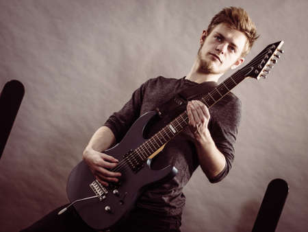 Young bearded man with electric guitar. Adult person is holding instrument and playing. Hobby, music...