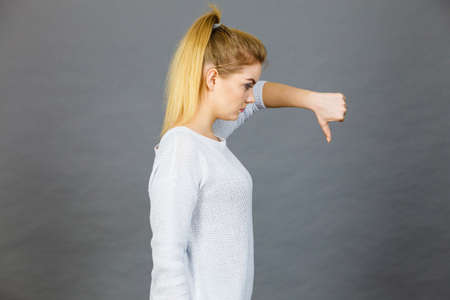 Unlike, dislike, failure gestures concept. Sad woman showing thumb down gesture, studio shot grey...