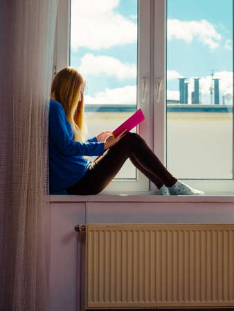 Leisure, literature and people concept. Young woman teen girl reading book at home while sitting on...