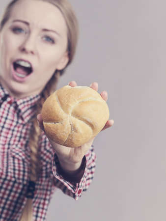 Displeased angry woman holding small bun bread roll. Bakery gluten products concept.