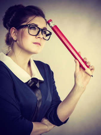 Student looking woman wearing nerdy eyeglasses holding big oversized pencil thinking about something.の写真素材