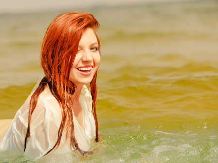 Summer fun, recreation outside concept. Redhead adult woman posing in water during summertime, having great time.の写真素材