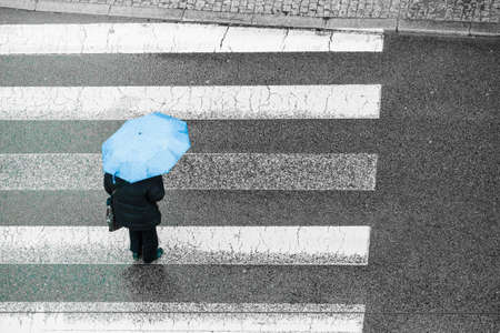 Person walking on city street during rainy day holding umbrella protecting from rain. High angle top view.の写真素材