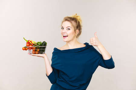 Buying healthy dieting food concept. Woman having many vegetables holding small shopping basket trolley.の写真素材