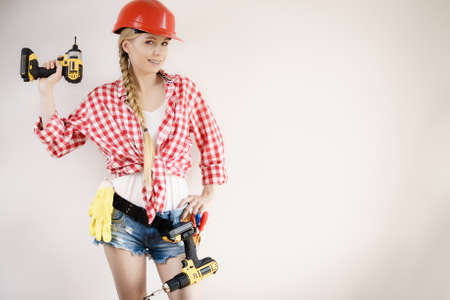 Young woman with toolbelt using driil and some power tools for her work at home. Girl working at flat remodeling. Building, repair and renovation.の写真素材