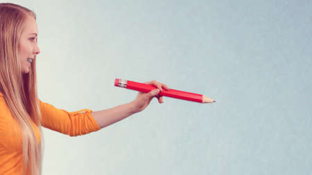 Teenage woman hand holding big pencil. Studio shot on light background with copyspace.の写真素材