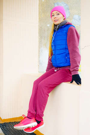 Woman wearing warm sportswear relaxing after exercising outside during cold weather.