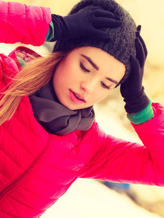 Young woman wearing winter clothes holding her head looking worried, outside shot during snowy weather.の写真素材