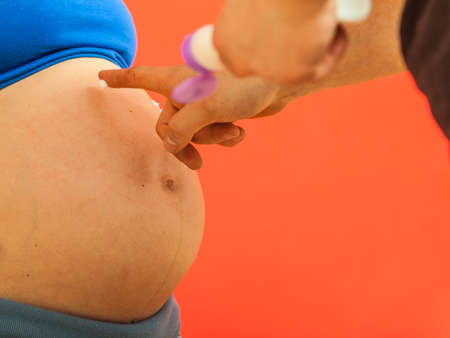 Skin care during pregnancy concept. Man applying cream on pregnant woman big bellyの写真素材