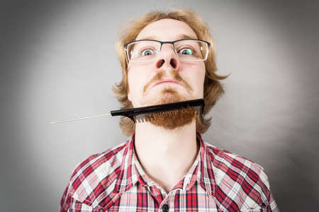 Bearded man having trouble with combing his beard using comb brush. Facial hair concept.の写真素材