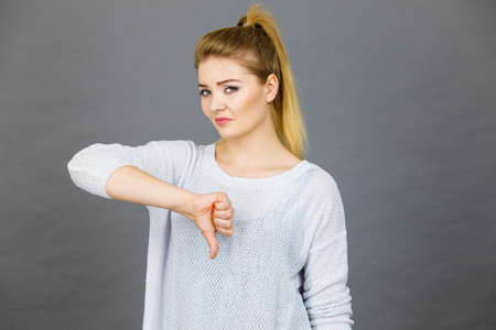 Unlike, dislike, failure gestures concept. Sad woman showing thumb down gesture, studio shot grey background.の写真素材