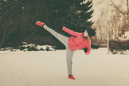 Outdoor sport exercising, sporty outfit ideas. Woman wearing warm sportswear training karate outside...
