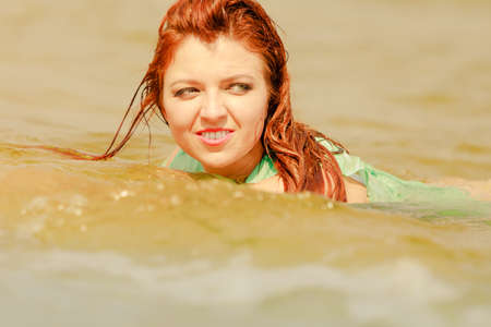 Summer fun, recreation outside concept. Redhead adult woman posing in water during summertime, having great time.の写真素材