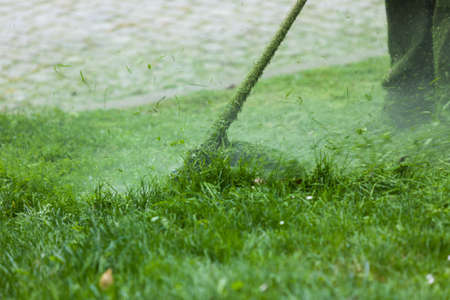 Man mowing green grass using brushcutter mower. Seasonal garden cleaning moder objects concept.