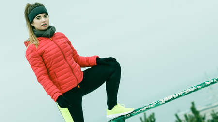 Outdoor sport exercises, sporty outfit ideas. Woman wearing warm sportswear training exercising stretching legs outside during winter. Cityscape panorama in backgroundの写真素材