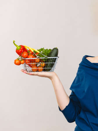 Lose weight, buying healthy food, vegetarian products. Hand holding shopping basket with vegetables, on greyの写真素材