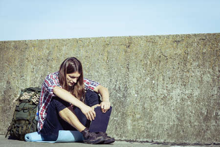 Man tourist backpacker relaxing outdoor sitting by grunge wall using tablet. Internet, tourism...