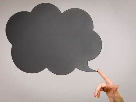 Woman hand pointing at black thinking or speech bubble empty for copyspace or text. Grey backgroundの写真素材