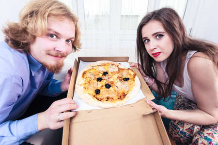 People, italian cuisine concept. Young couple at home eating hot fresh pizza from box. Delicious fast food meal delivered.の写真素材
