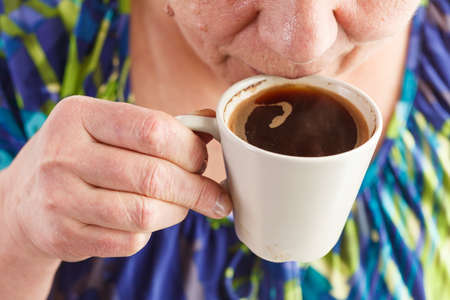 Elderly woman drinking hot drink at home. Senior pensioner female holding cup of coffee in their handsの写真素材