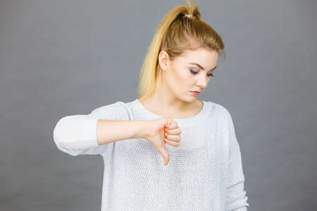 Unlike, dislike, failure gestures concept. Sad woman showing thumb down gesture, studio shot grey...