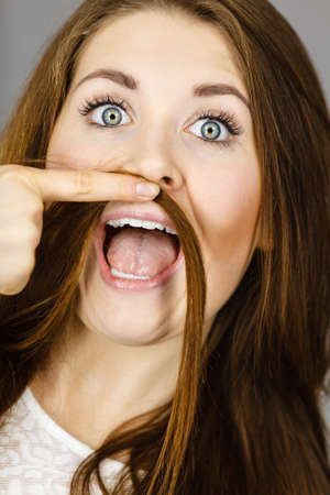 Woman having fun with her long brown hair making moustache being happy about hairdo condition,...