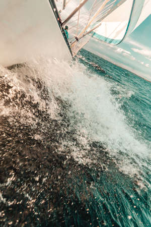 Yachting on sail boat bow stern shot splashing sea water. Sporty transportation conept.