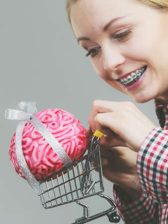 Happy woman holding shopping cart with brain inside. Clever, responsible buying concept.