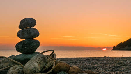 Beach stone fireplace with rope at sunrise. Sea water with rocks in the background. Vlychada Beach...