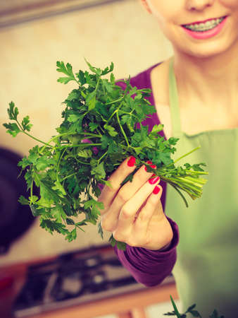 Healthy cooking using green natural herbs concept. Woman in kitchen holding parsley.の写真素材