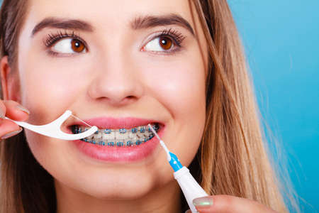Oral hygiene concept. Woman with braces cleaning teeth with toothbrush and dental flossの写真素材