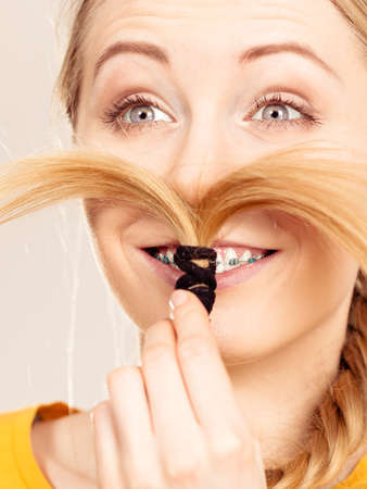 Woman making moustache out of braided blonde hair. Haircare, hairstyling having fun.
