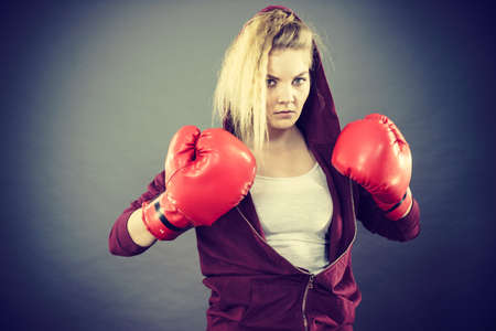 Sporty angry determined woman wearing red boxing gloves, fighting. Studio shot on dark background.の写真素材